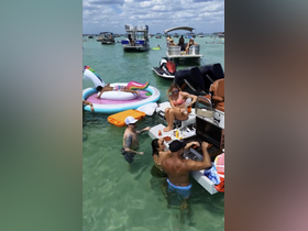 A lively group enjoys a fun day on the water, grilling and swimming around their boat, surrounded by friends and jet skis — the perfect summer party atmosphere.