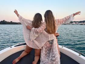 Two friends enjoy a picturesque moment on a boat, celebrating their time on the water with joyful gestures against a beautiful backdrop.