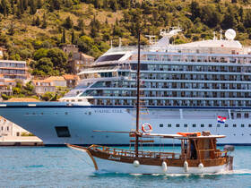 A picturesque view of a traditional wooden boat named 'Lorena' sailing in front of the modern cruise ship 'Viking Star' in a scenic harbor, showcasing the contrast between classic and contemporary vessels.