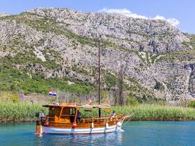 A charming wooden yacht navigates through serene waters, surrounded by lush greenery and rocky hills, showcasing the beauty of coastal Croatia.