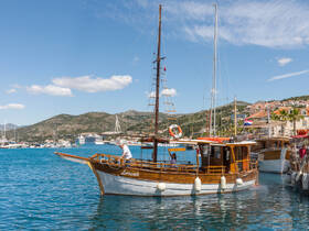 A beautifully crafted wooden boat named 'Lorena' docked in a picturesque harbor, showcasing the vibrant scenery of the surrounding hills and marina.