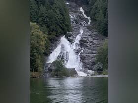 A stunning waterfall cascades down rocky cliffs, surrounded by lush greenery, showcasing the natural beauty of the landscape — perfect for nature lovers and scenic boat tours.
