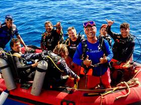 A joyful group of divers poses on a boat in the ocean, showcasing the excitement of underwater adventures and camaraderie in marine exploration.