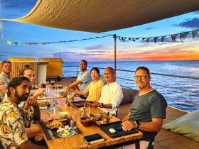 A lively group enjoys a sunset dinner on a boat, surrounded by stunning ocean views — perfect for memorable dining experiences at sea.