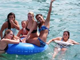 A lively group of friends enjoys a fun day in the water, lounging on a floating mat and celebrating together — perfect for summer adventures and beach parties.