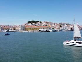A picturesque view of a catamaran sailing in a vibrant harbor, with the colorful cityscape of Lisbon in the background — perfect for exploring the beautiful coastline.