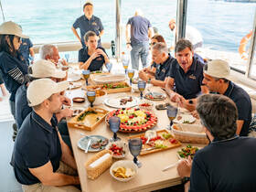 A group of guests enjoys a lavish meal aboard a boat, featuring a variety of dishes and drinks, perfect for onboard dining experiences.