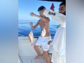 Two friends proudly display their catch while fishing on a boat, showcasing the excitement of a day on the water.