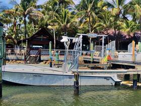 A sleek boat named 'High Note II' docked in a tropical setting, surrounded by palm trees and a lively waterfront restaurant, perfect for a day on the water.