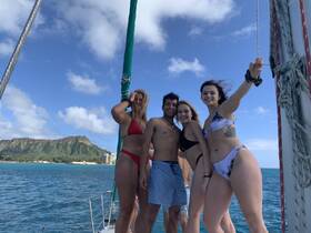 A cheerful group of friends poses on the deck of a sailboat, enjoying a sunny day at sea with stunning mountain views in the background — perfect for memorable sailing adventures.