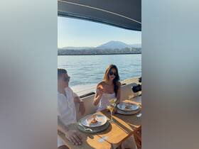 A couple enjoys a luxurious dining experience on a yacht, complete with cocktails and gourmet dishes, set against a stunning waterfront backdrop.