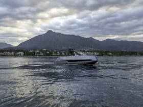 A sleek yacht glides through calm waters with a stunning mountain backdrop, showcasing the perfect blend of luxury and nature.