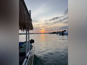 A couple relaxes on a pontoon boat as the sun sets over the water, creating a picturesque backdrop for a serene evening on the water.
