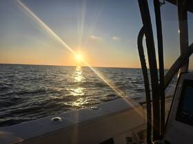 A serene sunset view from the deck of a boat, showcasing the tranquil ocean waters and the warm glow of the setting sun — perfect for evening cruises.