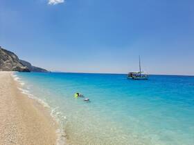 A swimmer enjoys snorkeling in the crystal-clear waters near a picturesque beach, with a sailboat anchored in the background — a perfect scene for summer adventures.