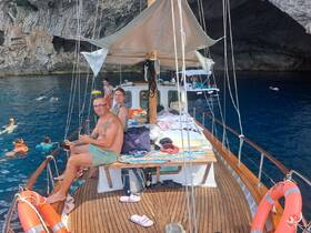 Guests relax on the deck of a boat while others enjoy swimming in the crystal-clear waters of a cave — a perfect day for snorkeling and exploration.