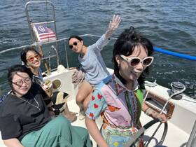 A lively group of friends enjoys a sunny day sailing, capturing joyful moments on the water while one takes the helm.