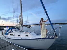 A woman poses elegantly on the bow of a sailboat at sunset, creating a picturesque scene perfect for celebrations or romantic outings on the water.