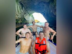 A group of friends enjoys a fun day on the water, posing inside a boat under a stunning cave formation — perfect for adventure seekers exploring beautiful coastal landscapes.