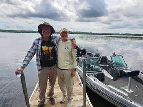 Two friends pose together on a dock beside their boat, ready for a day of fishing and adventure on the water.