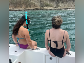 Two friends prepare for a snorkeling adventure while sitting on the edge of a boat, enjoying the beautiful waters and scenic backdrop.