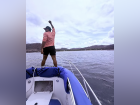 A person stands triumphantly on the bow of a boat, enjoying the scenic views — a perfect moment of celebration on the water.