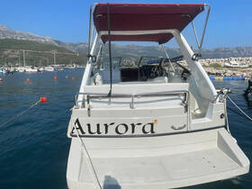 The rear view of the 'Aurora' boat docked in a serene marina, showcasing its sleek design against a backdrop of mountains and other vessels.