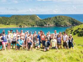 A vibrant group of travelers poses for a photo against a stunning coastal backdrop, capturing the essence of adventure and camaraderie during their island hopping experience.