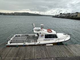 A view of the 'Predator' boat docked at the waterfront, showcasing its structure and design against a cloudy backdrop.