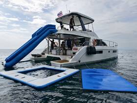 A luxurious catamaran features a fun inflatable slide and floating mats, perfect for water activities and relaxation on the open sea.