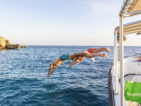A group of friends joyfully dives into the crystal-clear waters from a boat, capturing the essence of summer fun and adventure on the water.