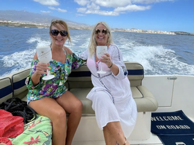 Two friends enjoy cocktails on a boat, celebrating their day on the water with stunning views in the background — perfect for memorable outings.