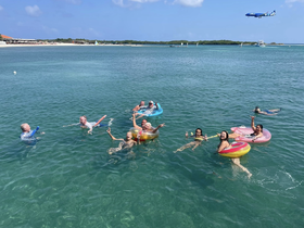 A lively group enjoys a fun day in the water, floating and swimming together in a beautiful beach setting — perfect for summer adventures and group outings.