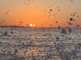 A stunning sunset reflected on the water, captured through splashes, creating a beautiful and dynamic scene perfect for evening boat trips.