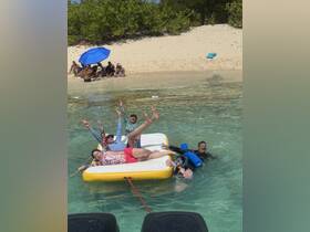 A lively group enjoys a fun day on a floating mat in shallow waters, showcasing the perfect beach experience with swimming and laughter.