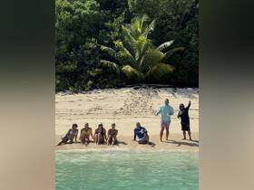 A lively group enjoys a beach day, relaxing on the sand with drinks in hand — perfect for celebrating special moments in a tropical paradise.