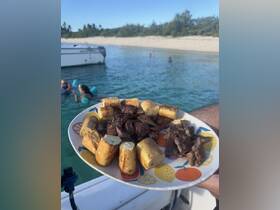 A delicious spread of grilled meat and bread rolls served on a plate, perfect for enjoying snacks while anchored near a sandy beach.