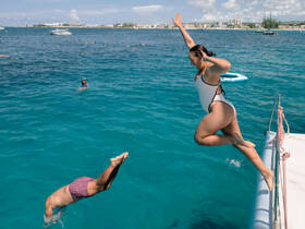 Two friends enjoy a thrilling moment as one jumps into the vibrant turquoise waters while the other swims nearby, showcasing the excitement of water activities on a sunny day.