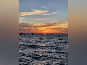 A stunning sunset over the water, with silhouettes of boats in the distance, creating a picturesque scene perfect for evening cruises.