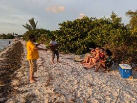 A lively group enjoys a beach celebration with music at sunset, creating a perfect atmosphere for fun and relaxation by the water.