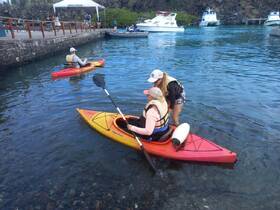 Two women engage in kayaking, with one assisting the other in the water — a perfect snapshot of adventure and teamwork on a beautiful day.