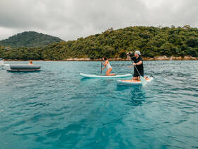 Two individuals enjoy paddleboarding in crystal-clear waters, surrounded by lush greenery — a perfect day for water activities and fun in the sun.
