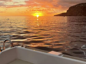 A serene sunset view from the deck of a boat, showcasing the tranquil waters and distant cliffs — perfect for romantic evening cruises.