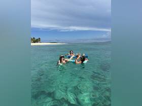 A lively group enjoys a refreshing day in the crystal-clear waters, relaxing on floats with cocktails in hand — the perfect beach getaway.