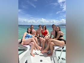 A lively group of friends enjoys a sunny day on a boat, celebrating with drinks and laughter in the beautiful turquoise waters.