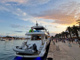 A stunning sunset view of a yacht docked at a bustling harbor, with people enjoying the vibrant atmosphere along the waterfront.