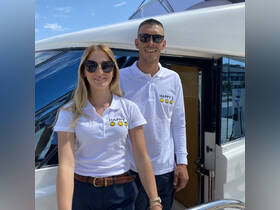 Two individuals pose in front of a boat, showcasing a cheerful atmosphere. The image captures the essence of hospitality in a boating context.