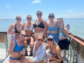 A lively group of friends enjoys a sunny day on the water, celebrating with drinks and smiles — perfect for a fun day out on a boat.