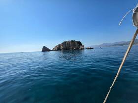 A serene view of a rocky island surrounded by calm waters, with small boats visible in the distance — a perfect representation of coastal exploration.