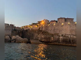 A picturesque evening view of a coastal town illuminated by warm lights, reflecting beautifully on the water — a perfect backdrop for a serene boating experience.
